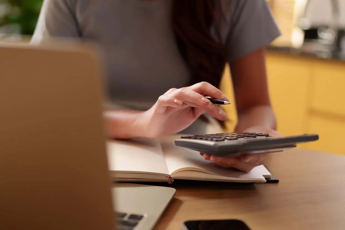 A person using a calculator to determine the Airbnb profit formula and estimate earnings for a rental property