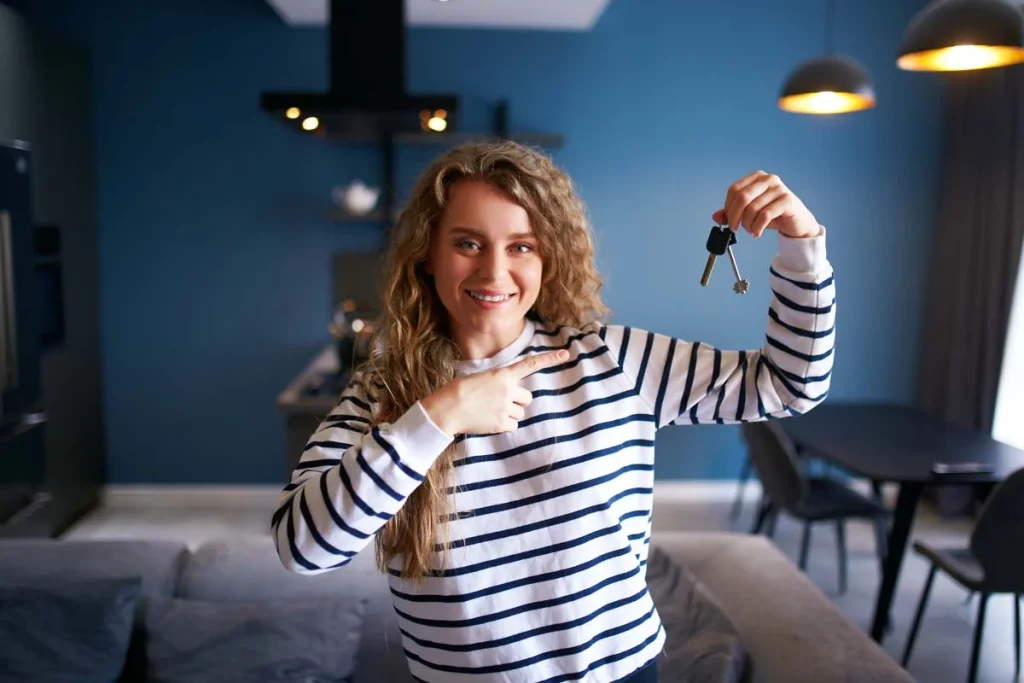 A person holding house keys in a bright, modern living room representing new property management
