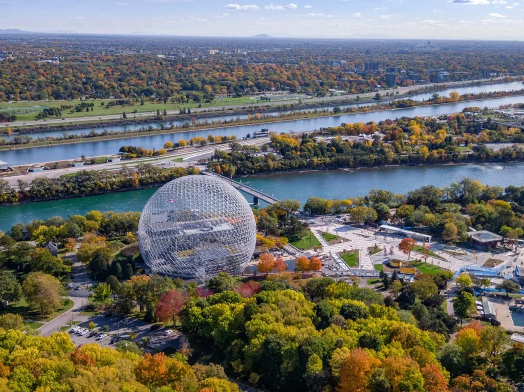 A scenic daytime view of Montreal, Quebec, Canada, showing the architectural landmark Biosphere Environment Museum and maple trees changing color in the fall season