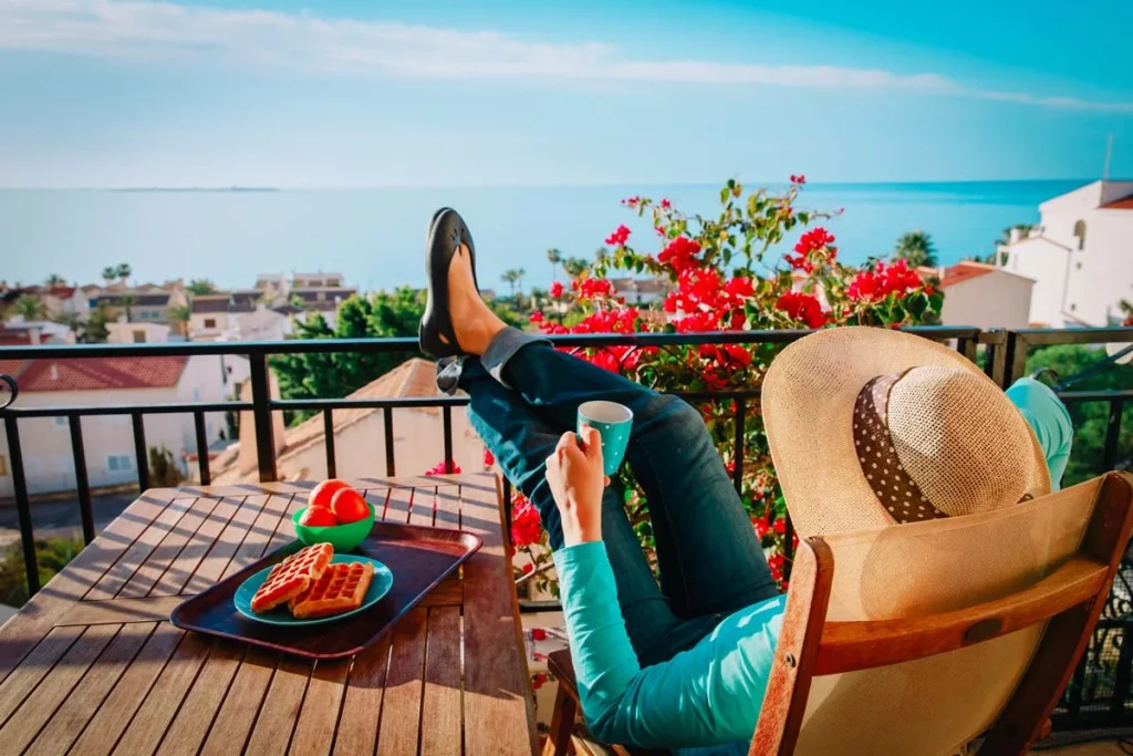 A happy guest relaxing on a balcony overlooking the ocean, enjoying the benefits of professional Airbnb management