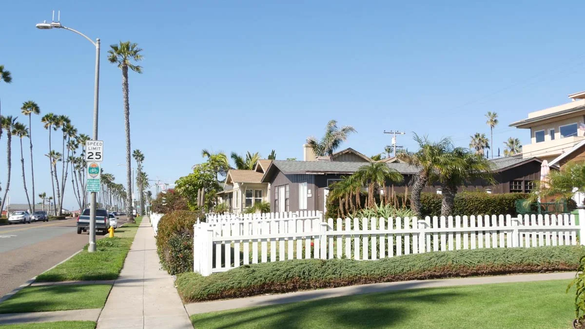 A sunny residential neighborhood street in Los Angeles with a house and palm trees