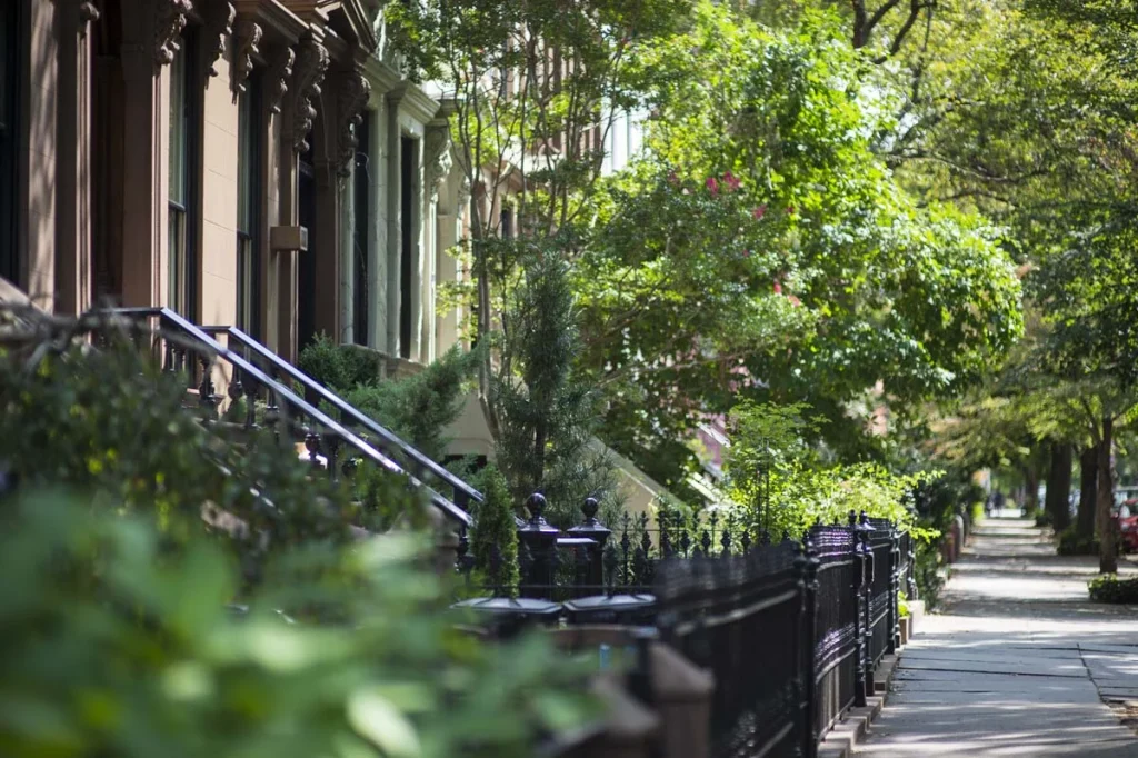 A tree-lined residential street in Manhattan featuring classic brownstone apartment buildings