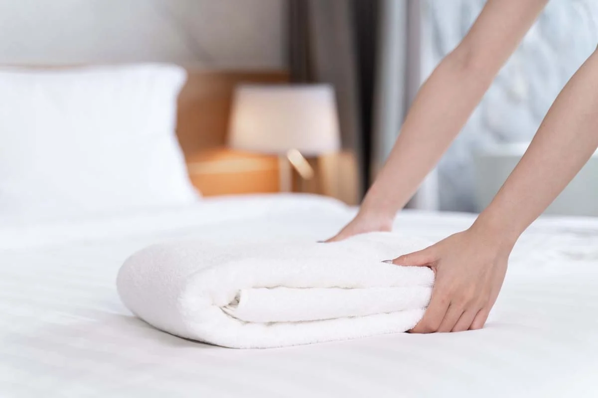 A close-up of a neatly made bed with white linens and fresh towels in a managed rental property