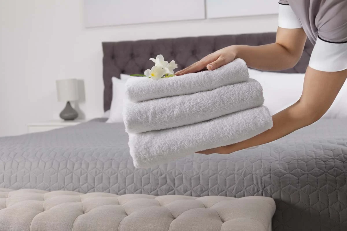 A cleaner placing fresh towels on a bed in a rental room