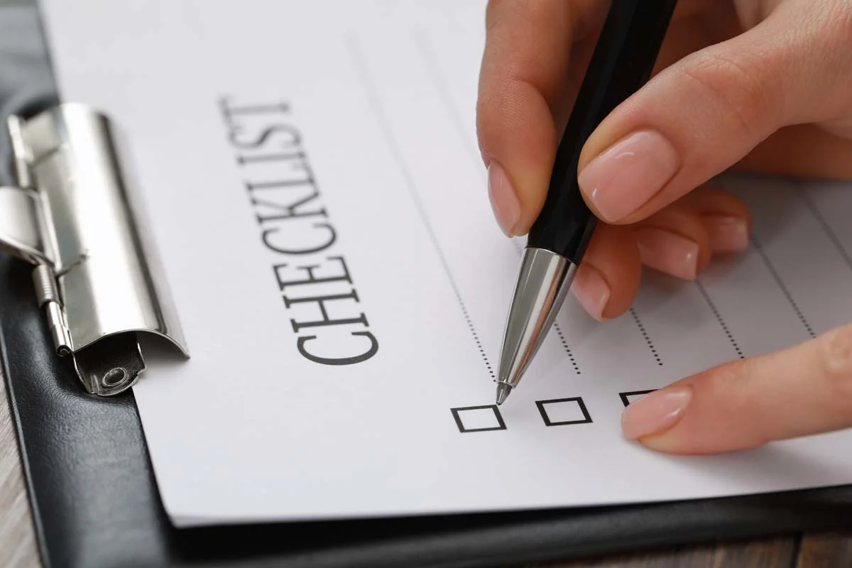 A close-up of a clipboard with a printed checklist and a pen on a wooden desk