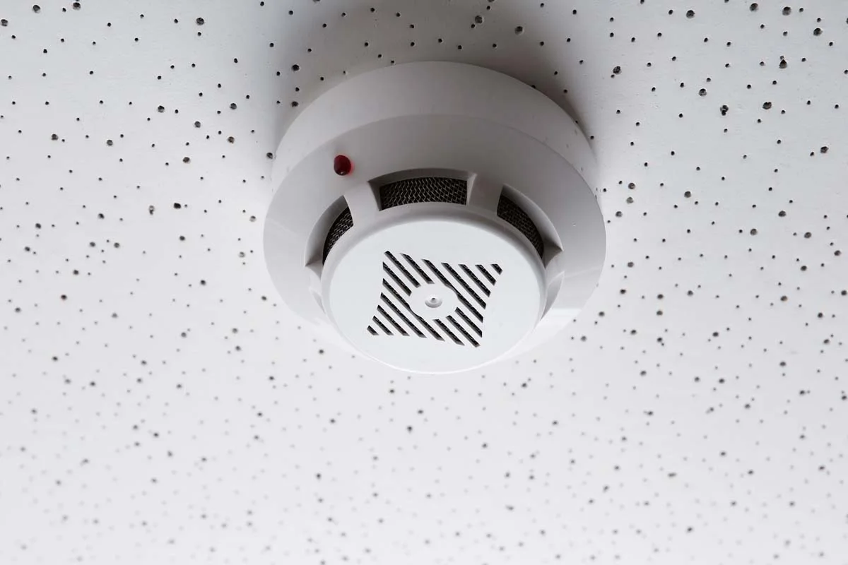 A modern smoke and carbon monoxide detector mounted safely on a white ceiling