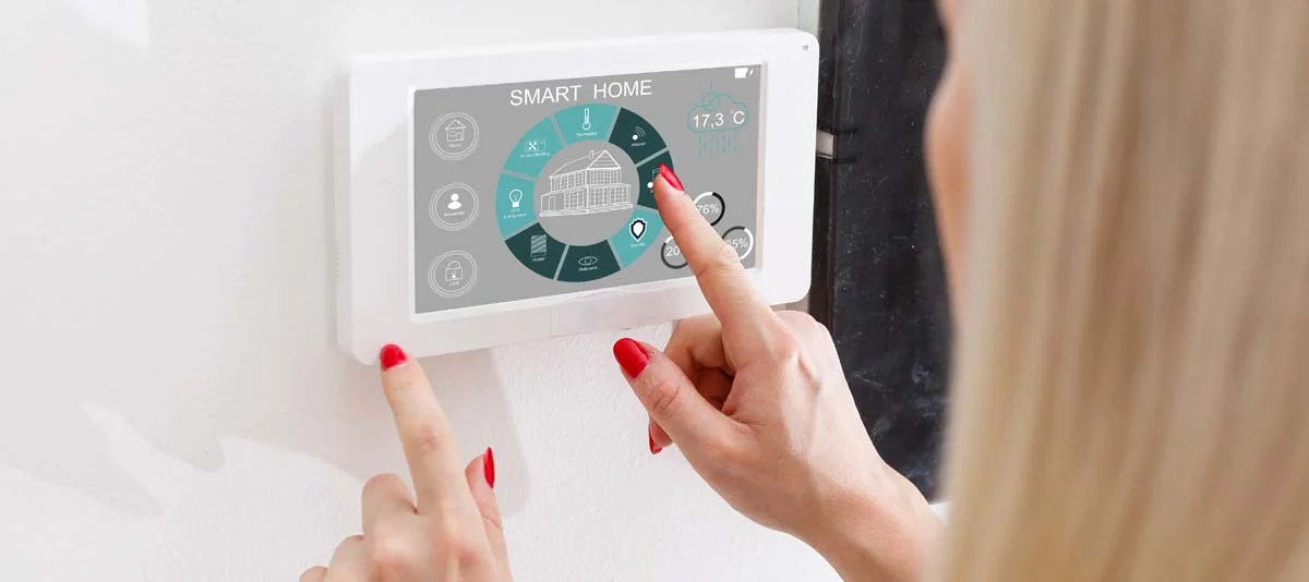 A person adjusting a modern smart thermostat on a wall to manage home energy efficiency