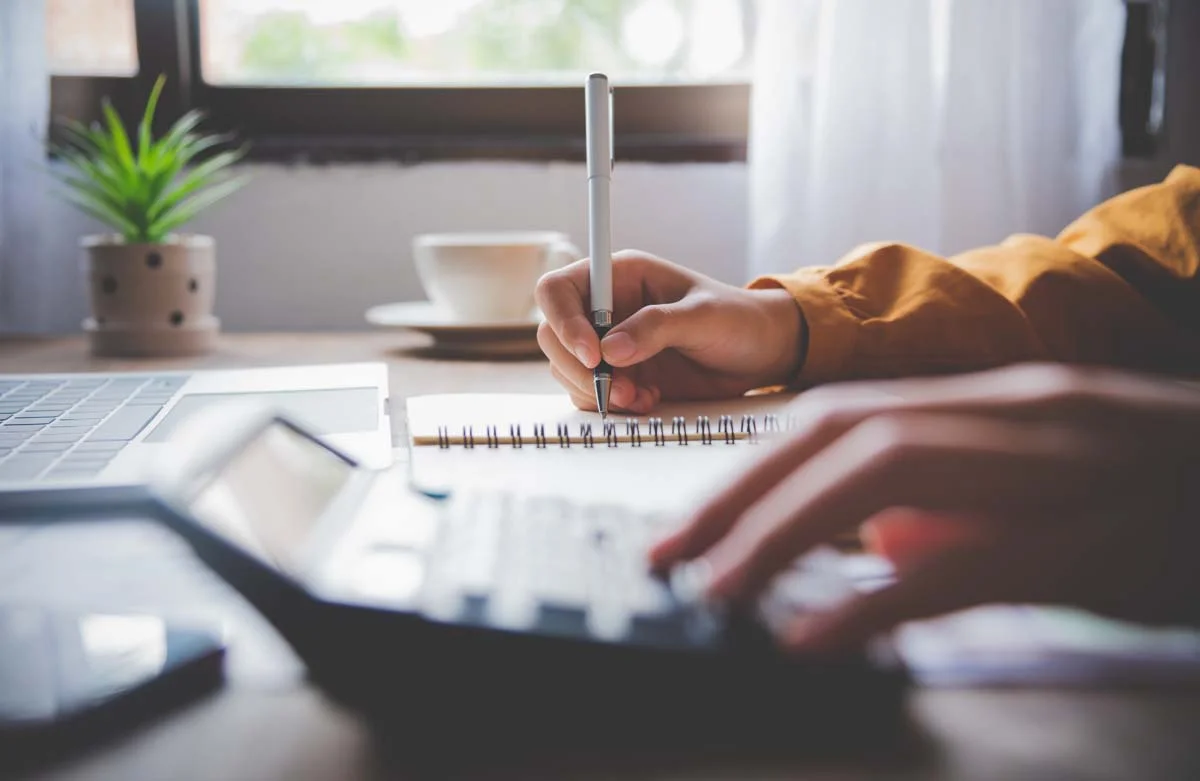A person using a calculator with paperwork on a desk to represent the permit application process
