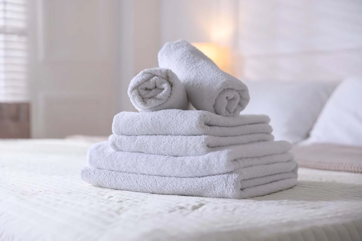 A stack of freshly folded white towels resting on a neatly made bed in a vacation rental