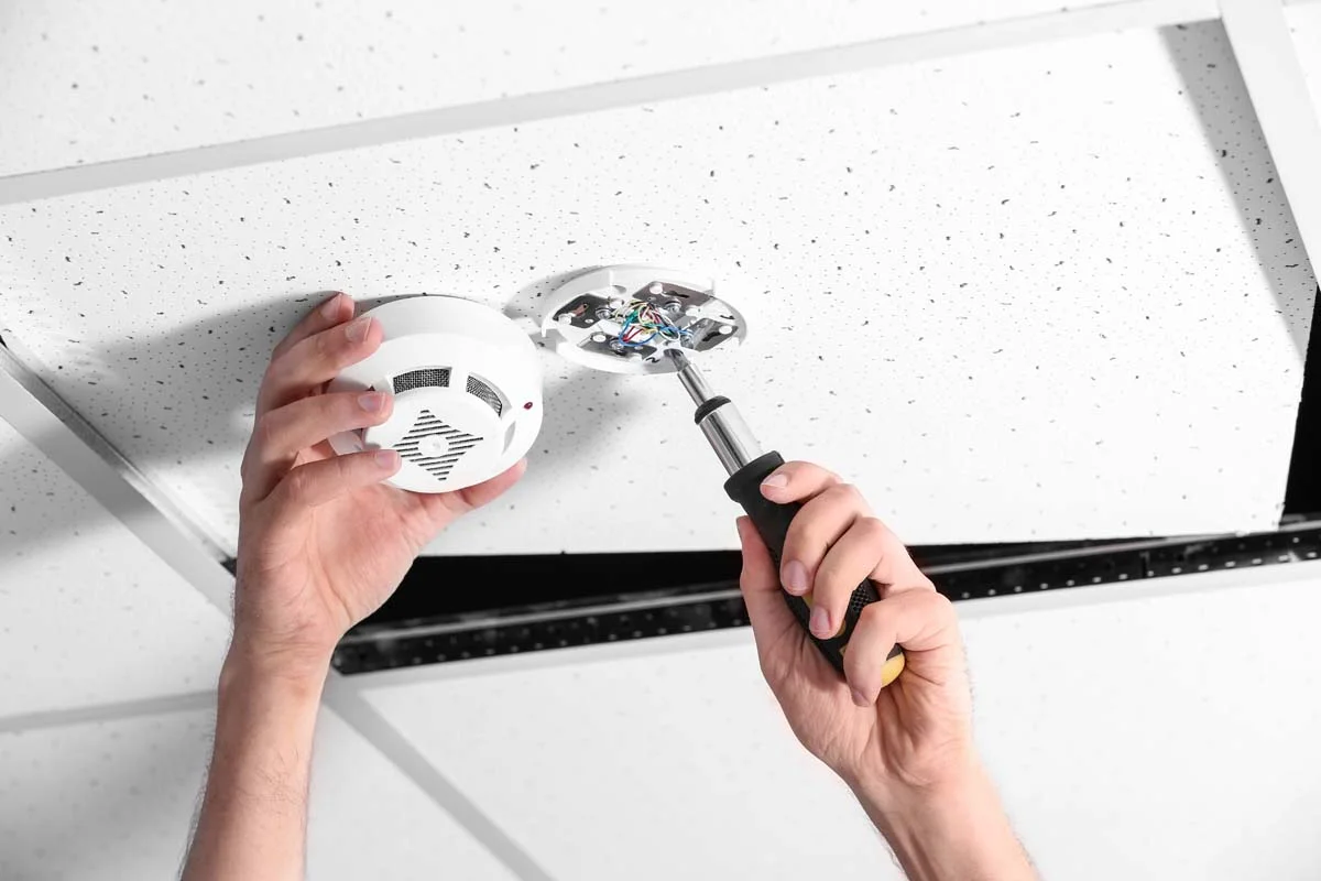 A white residential smoke and carbon monoxide detector installed on a ceiling for guest safety