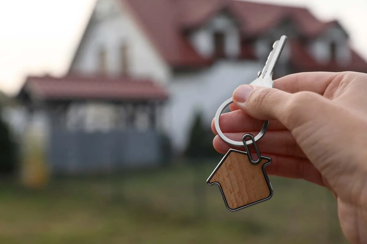 Close-up of house keys being held in front of a modern residential rental property