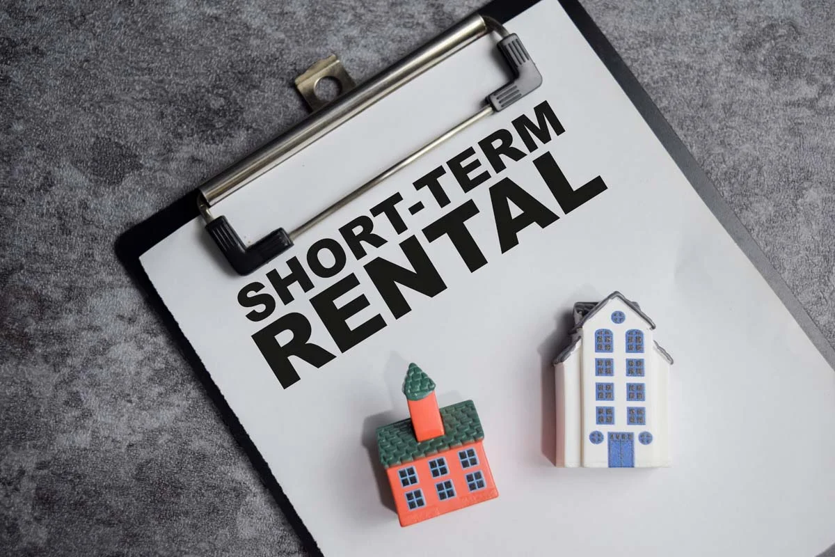 Concept of short-term rental written on a clipboard with miniature houses