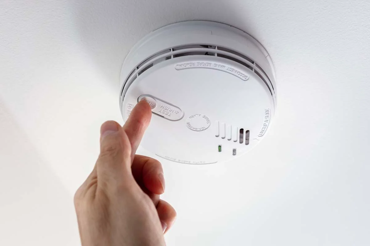 Hand pressing the test button on a modern residential smoke and carbon monoxide alarm