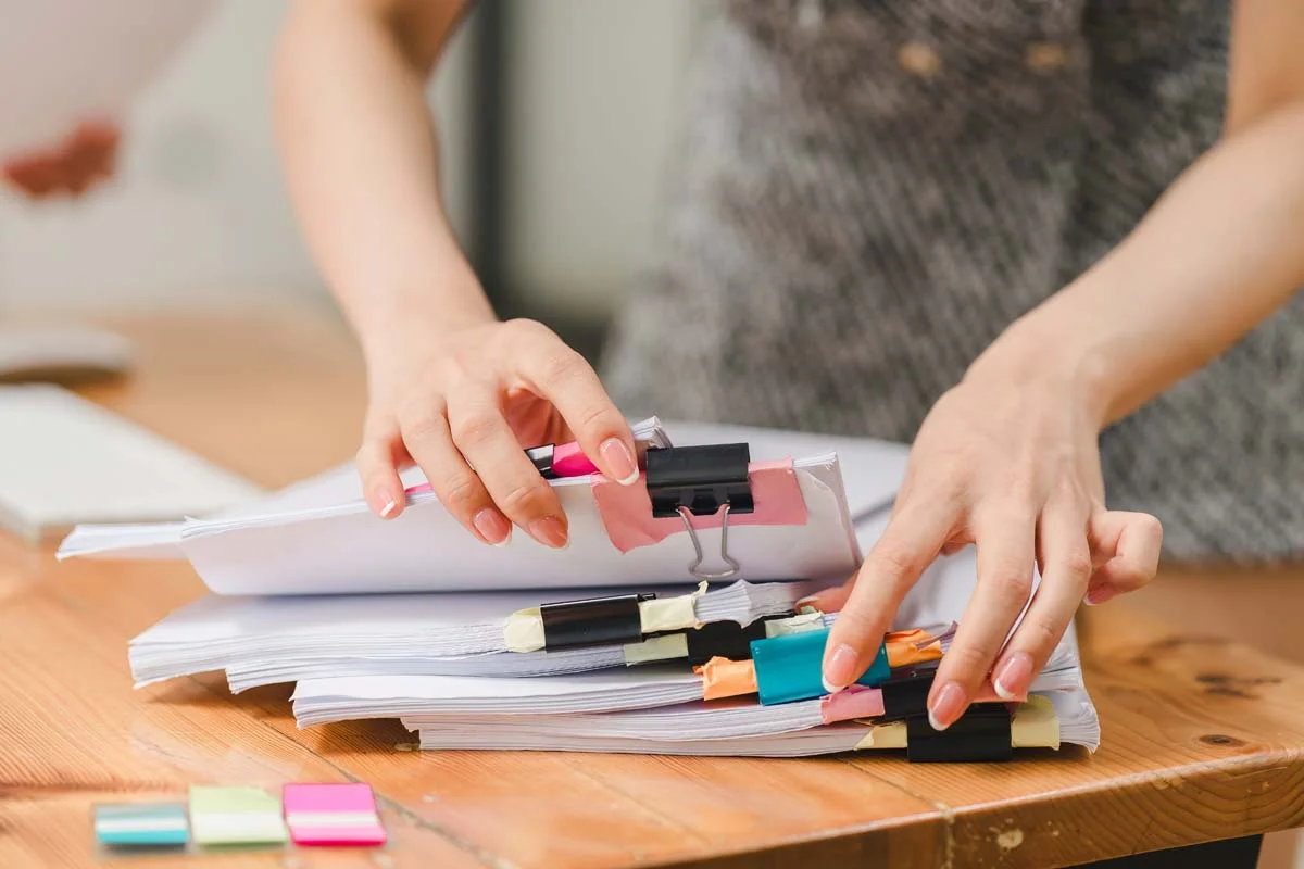 Hands organizing paperwork and official documents on a desk next to a laptop