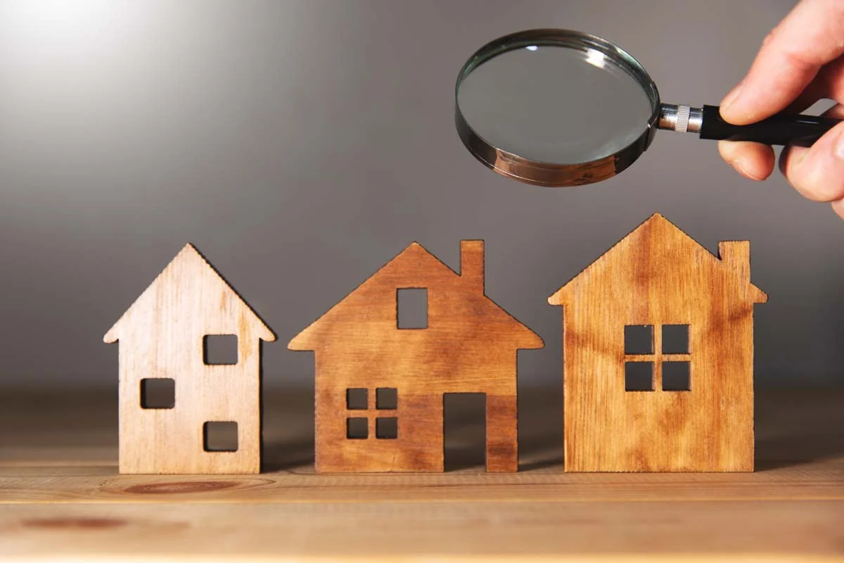 Magnifying glass and miniature wooden houses, representing short-term rental license inspection