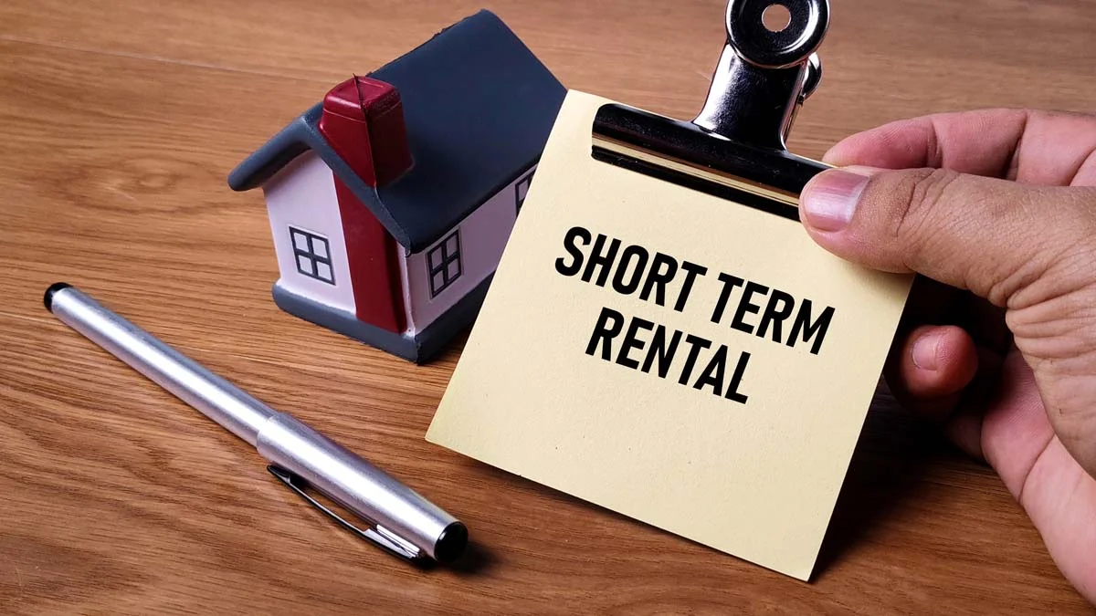 Miniature house, a pen, and a piece of paper with the words “short term rental” printed on it