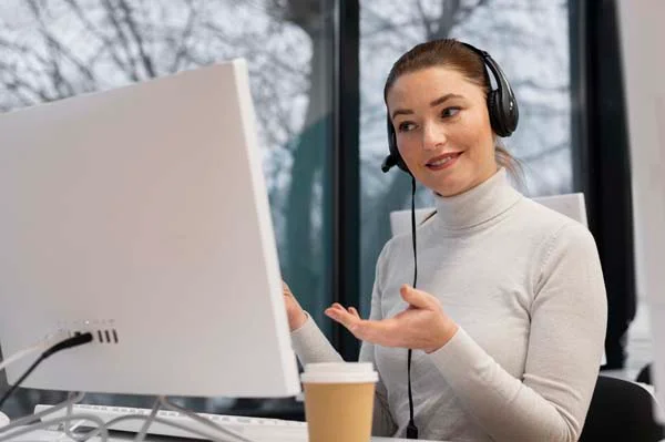 A cheerful guest service agent with a headset typing on a laptop to handle traveler communications