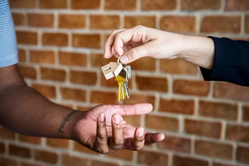 A close-up view of hands extending a set of house keys toward the camera inside a warm, modern entryway