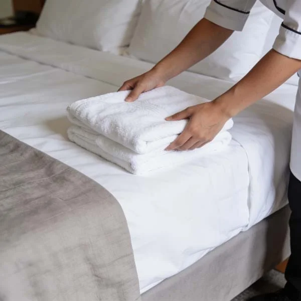 Professional cleaner placing fresh white towels on a neatly made bed in a rental property