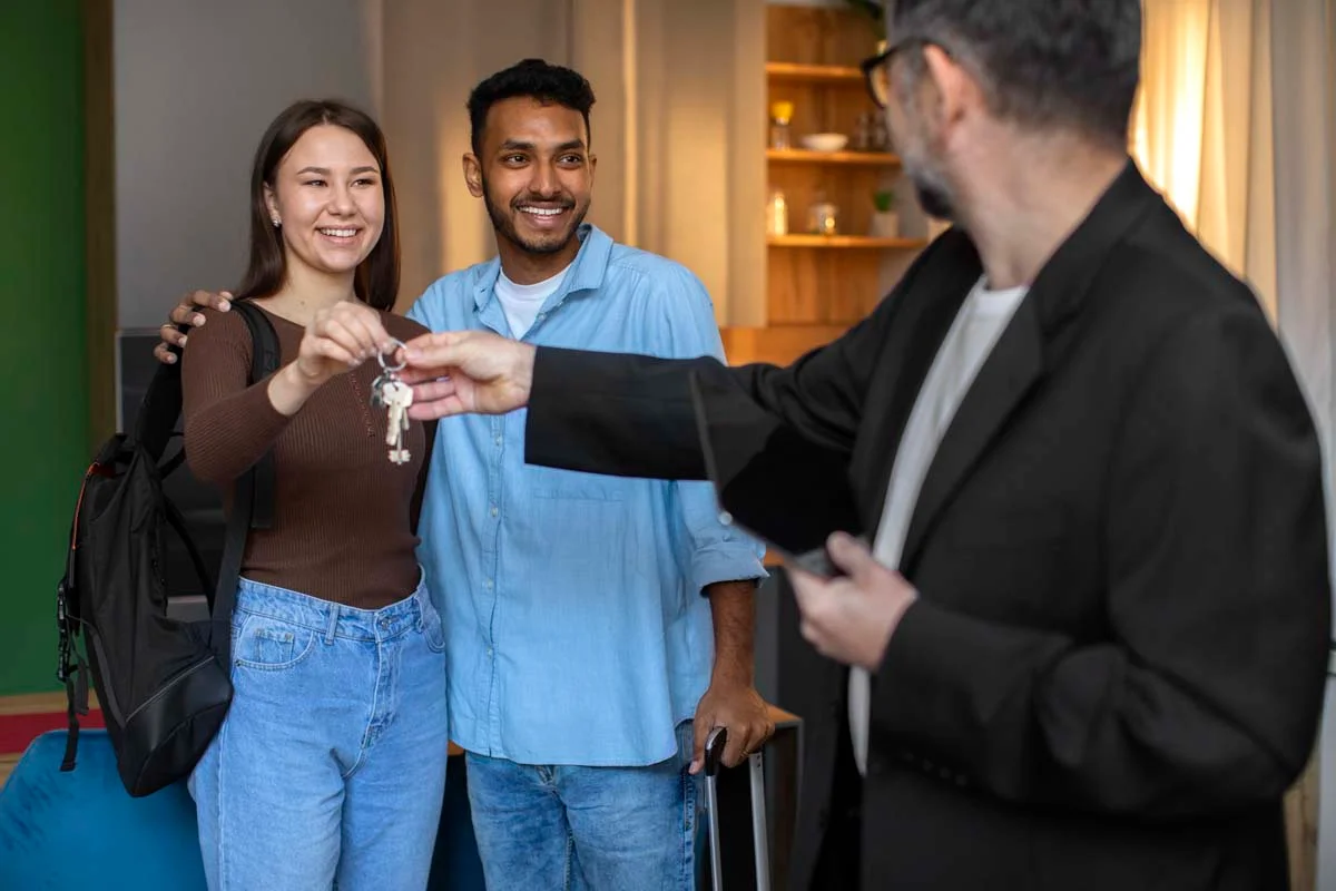 A professional property manager handing house keys to smiling guests at the front door