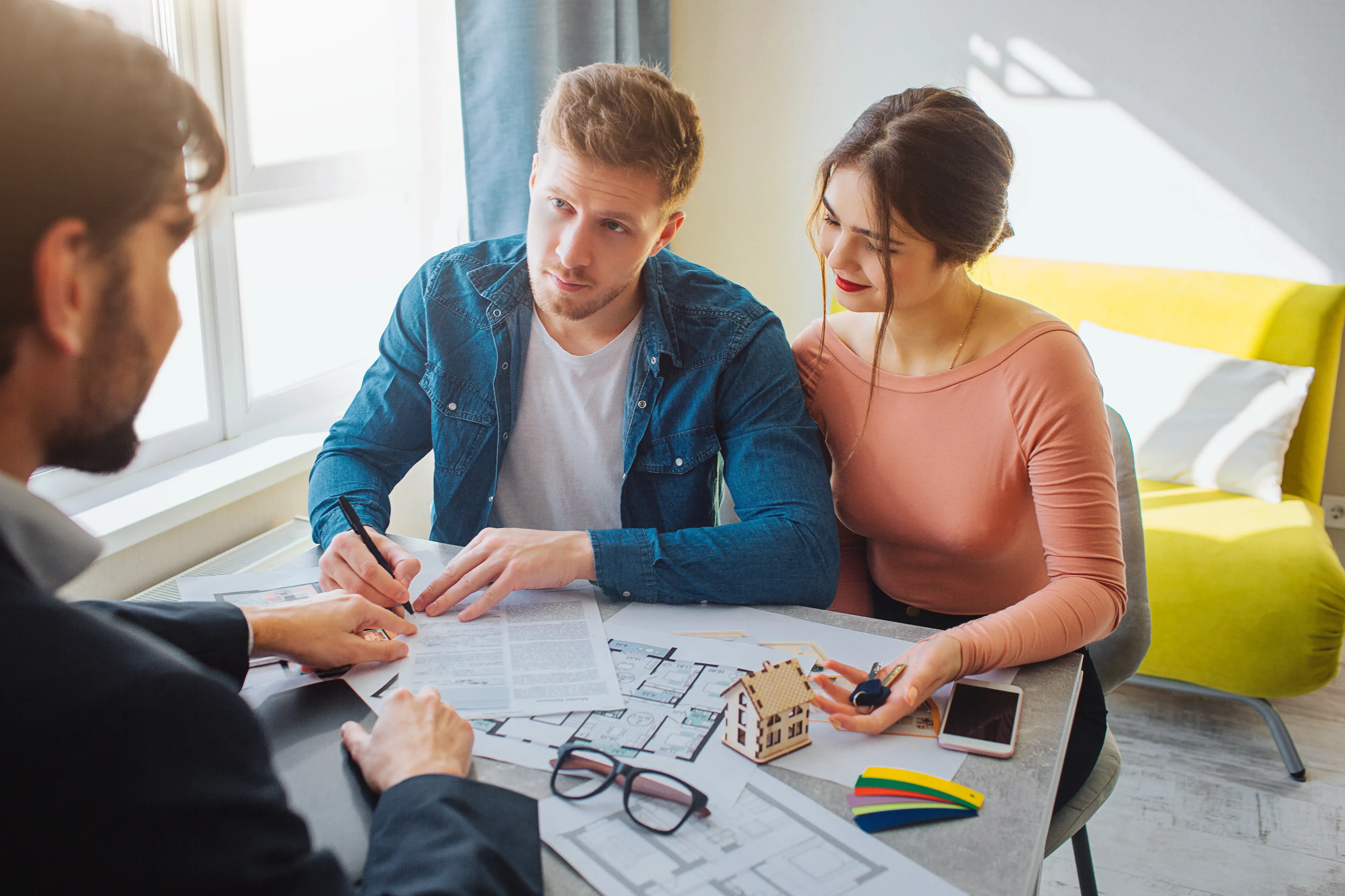 Couple reviewing property details on a tablet with an advisor, with floor plans on the table in front of them