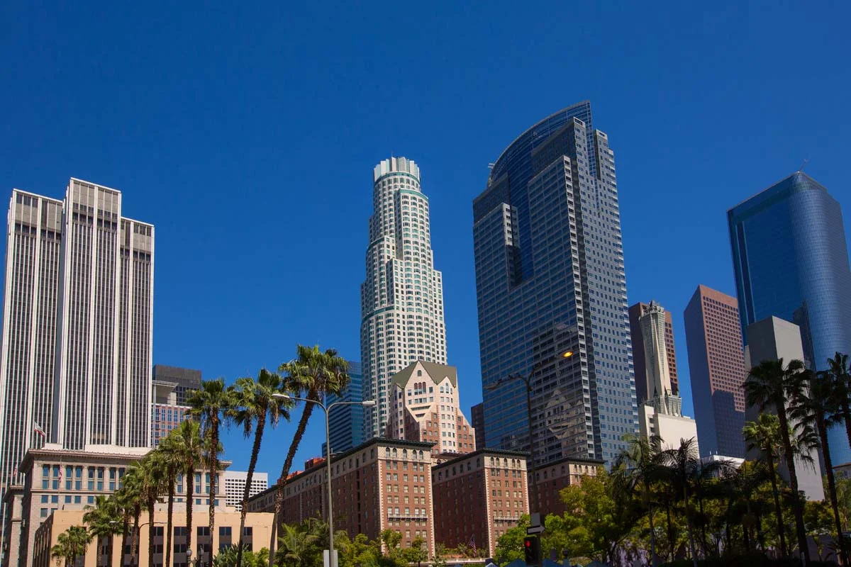 Downtown Los Angeles skyline with modern skyscrapers, green spaces, and city streets under a clear blue sky