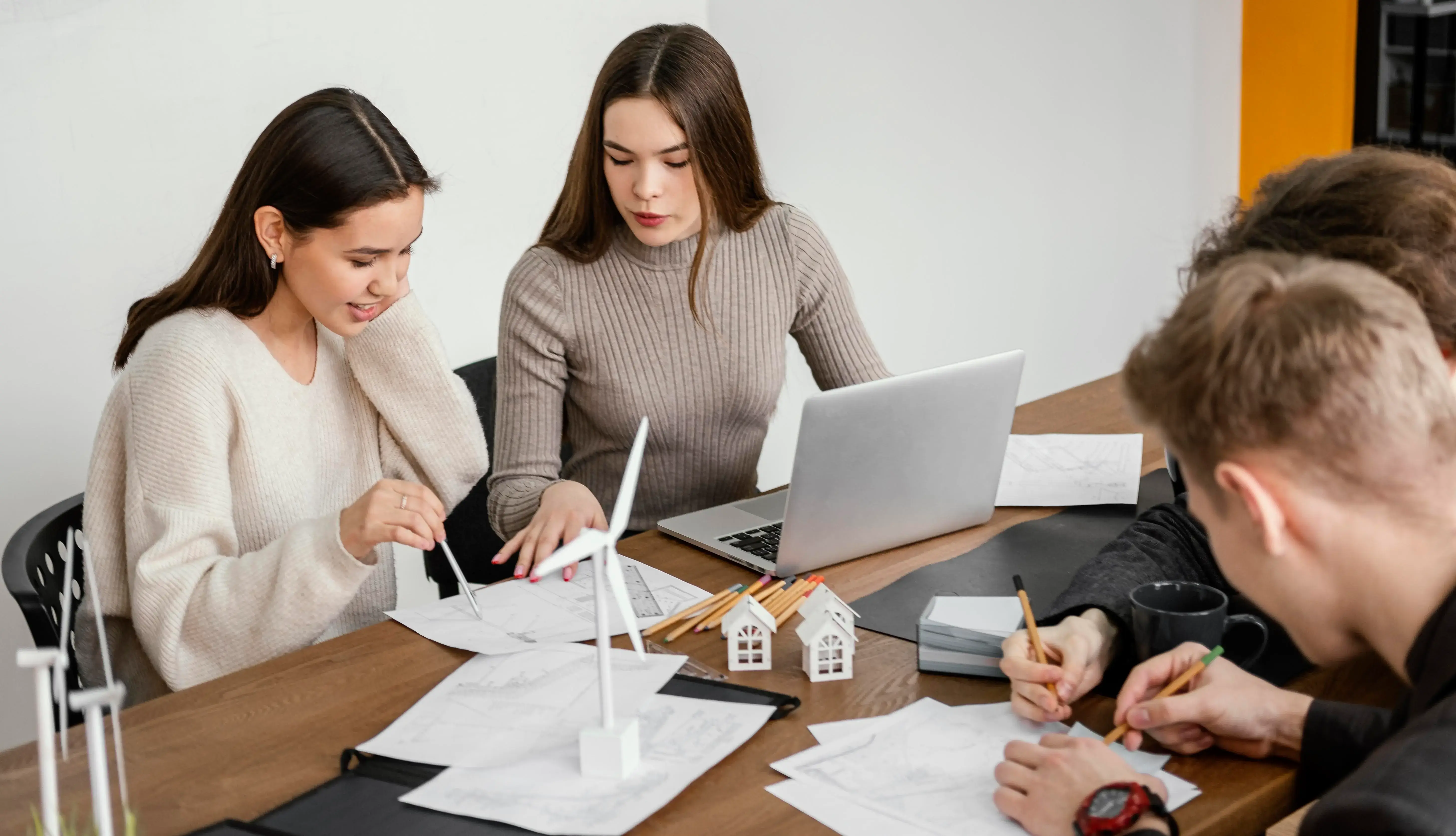 People discussing property investment around a desk with building models, charts, and a laptop