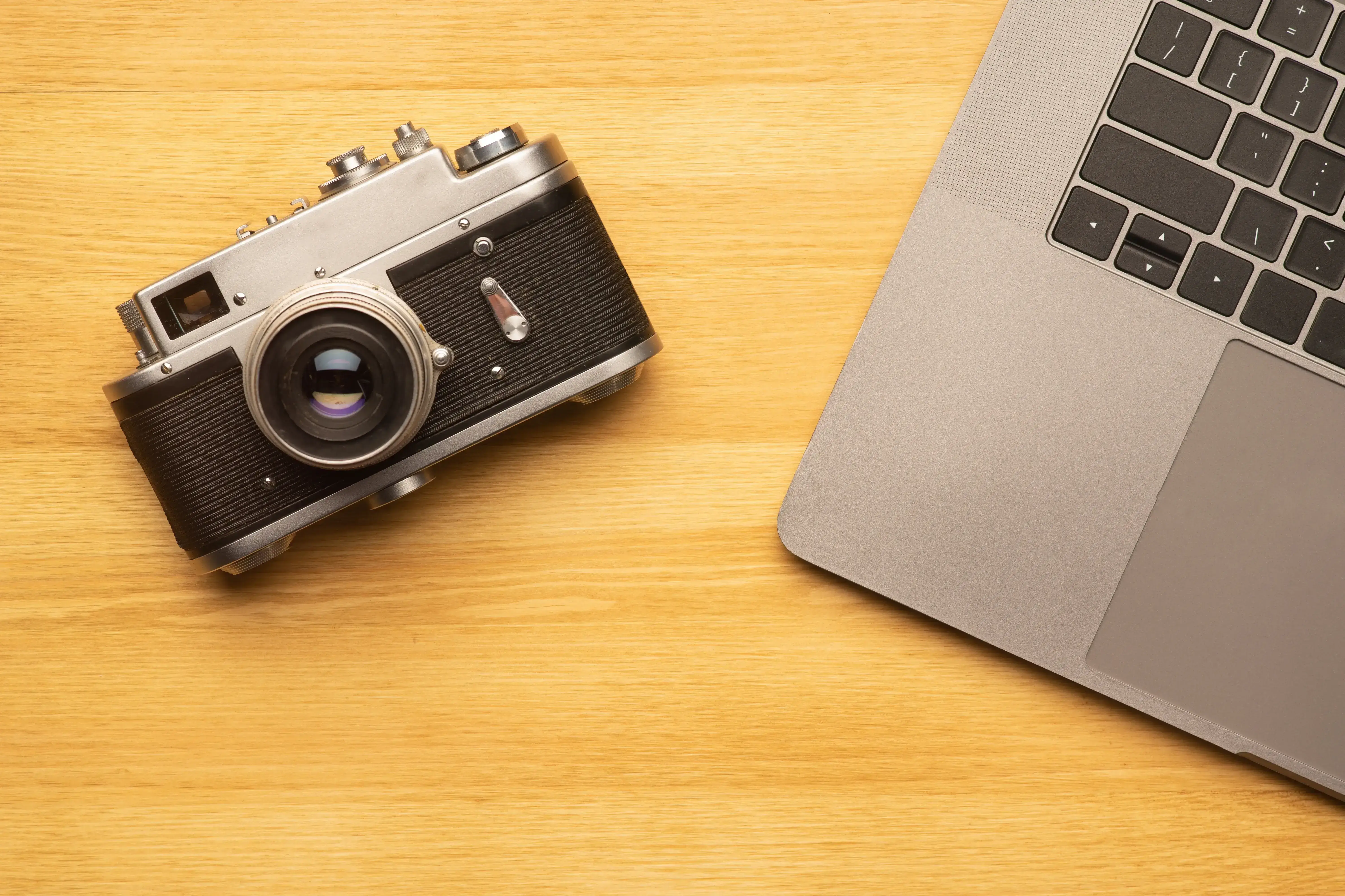 A camera and laptop resting side by side on a desk, shown in close-up