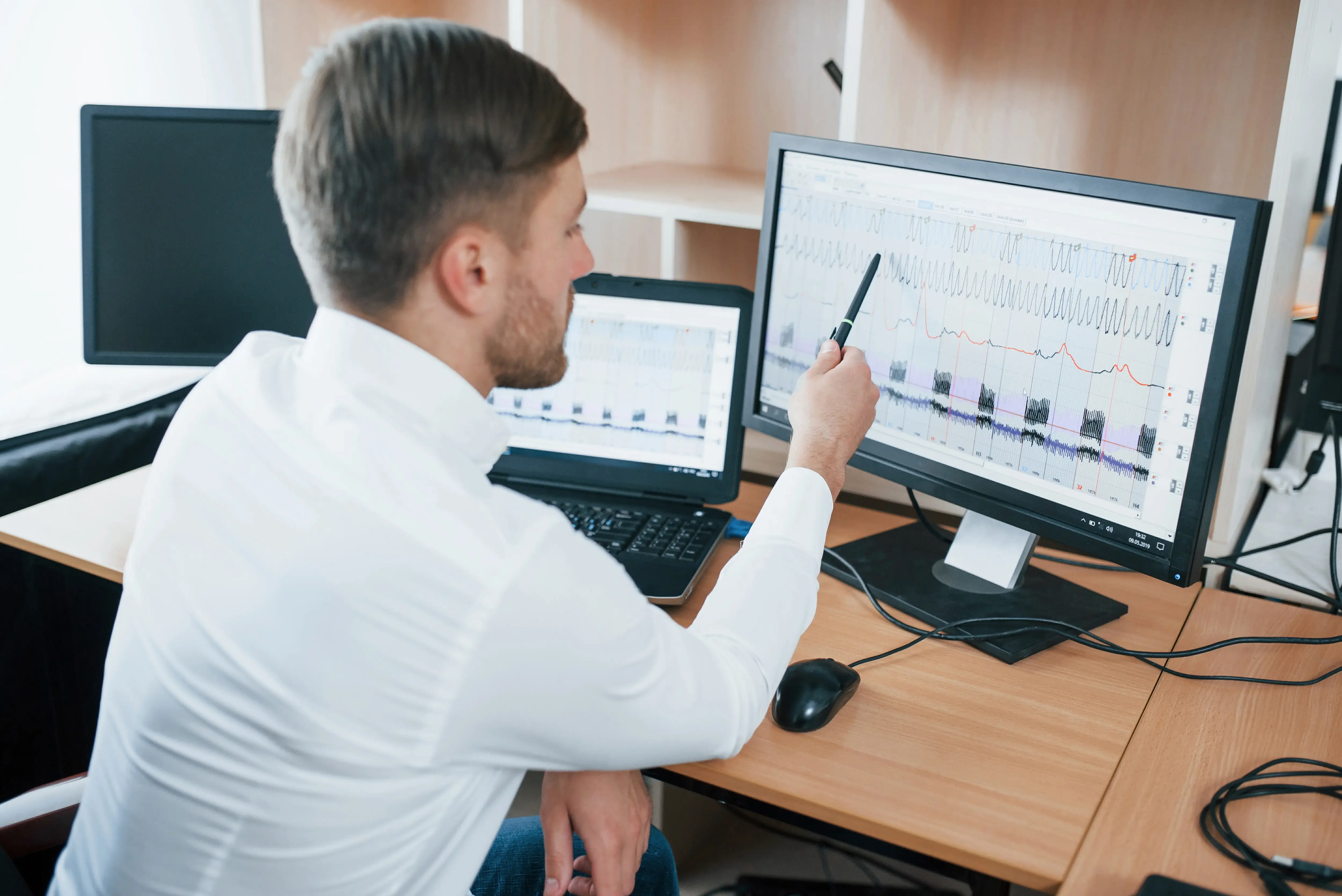 A man managing data in front of a desk with data graphs on screen.
