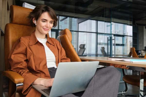A professional woman smiling while working on her laptop in an office setting