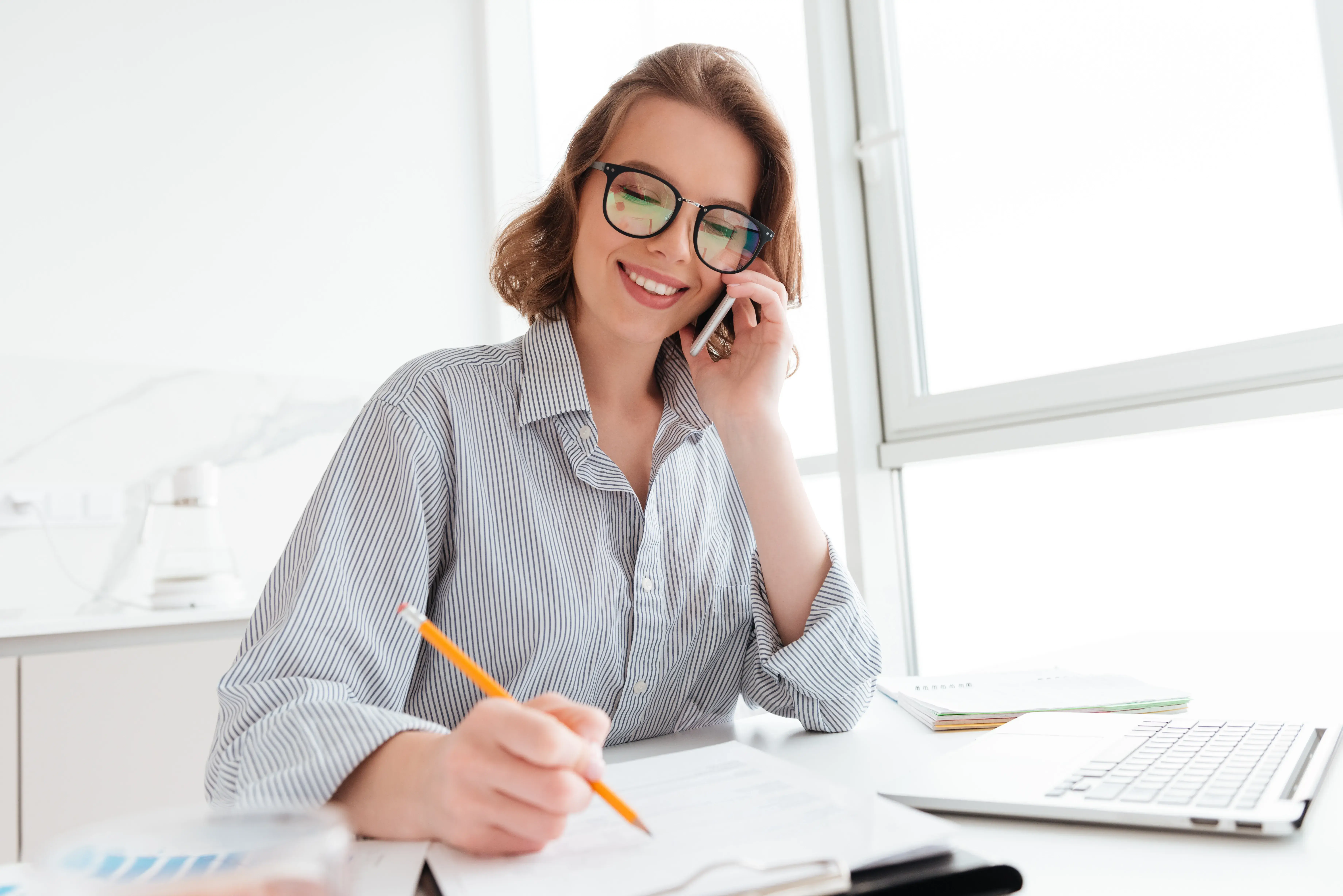A woman working at a desk in a bright office while on a phone call.