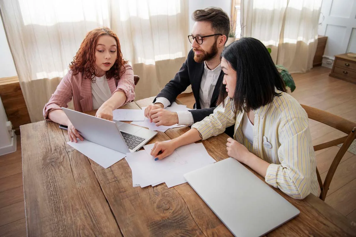 A young couple reviewing paperwork with a financial advisor or real estate agent in a living room