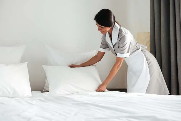 Professional housekeeper preparing fresh bed linens in a short-term rental bedroom