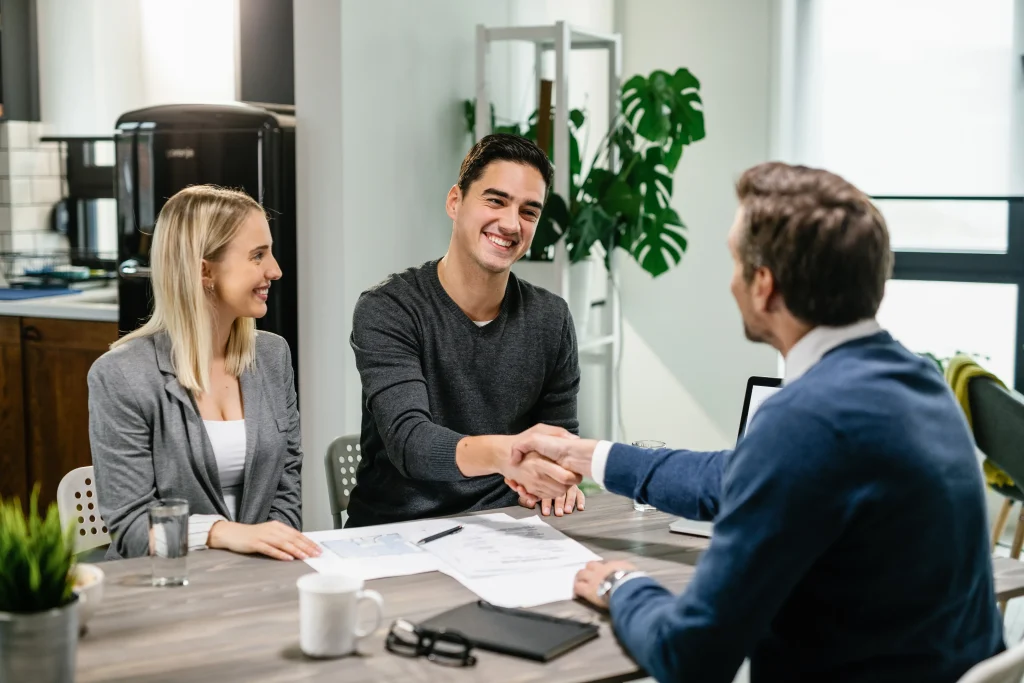 Smiling couple shaking hands with a professional advisor during a meeting.