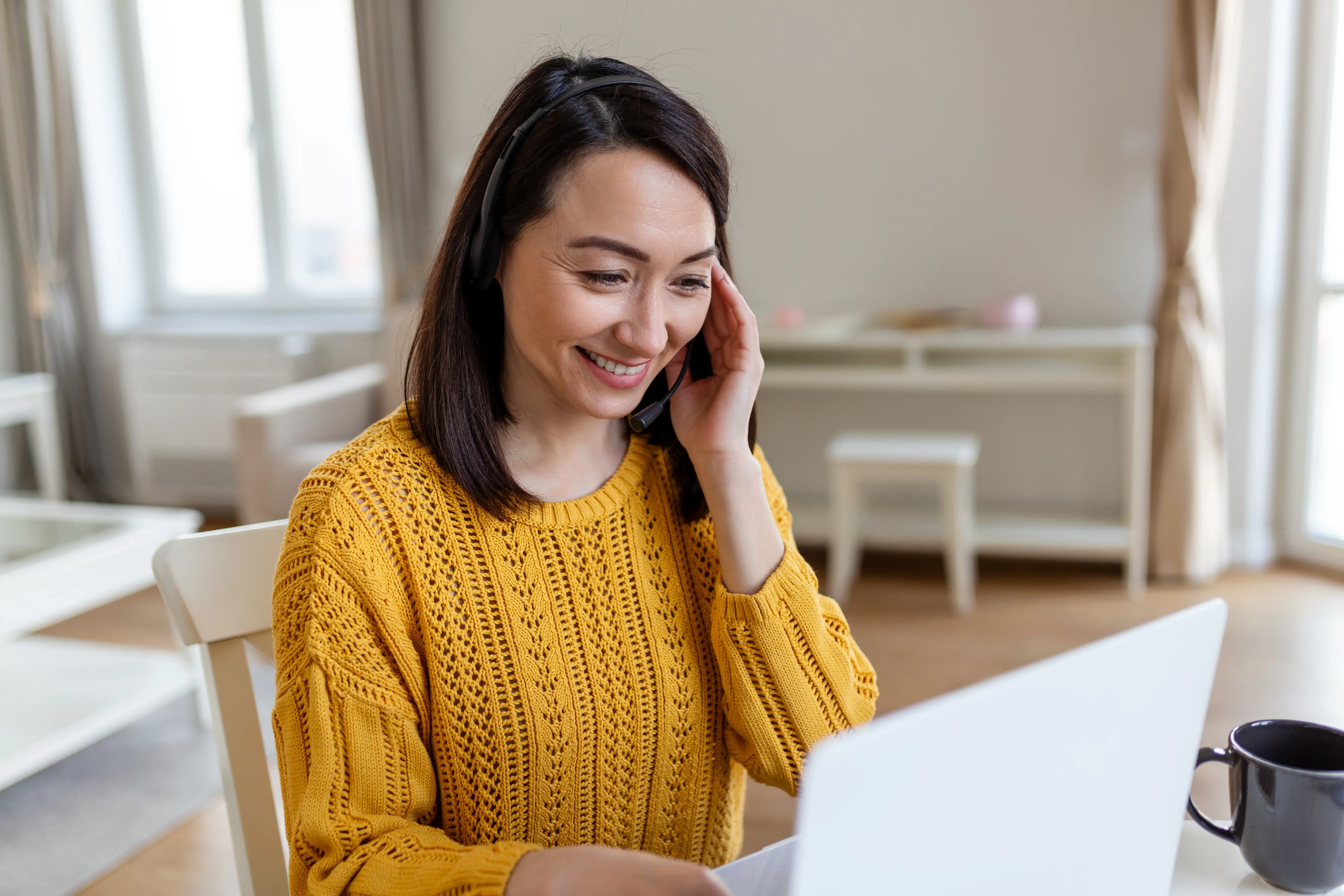 Smiling woman working on a laptop while talking on the phone.