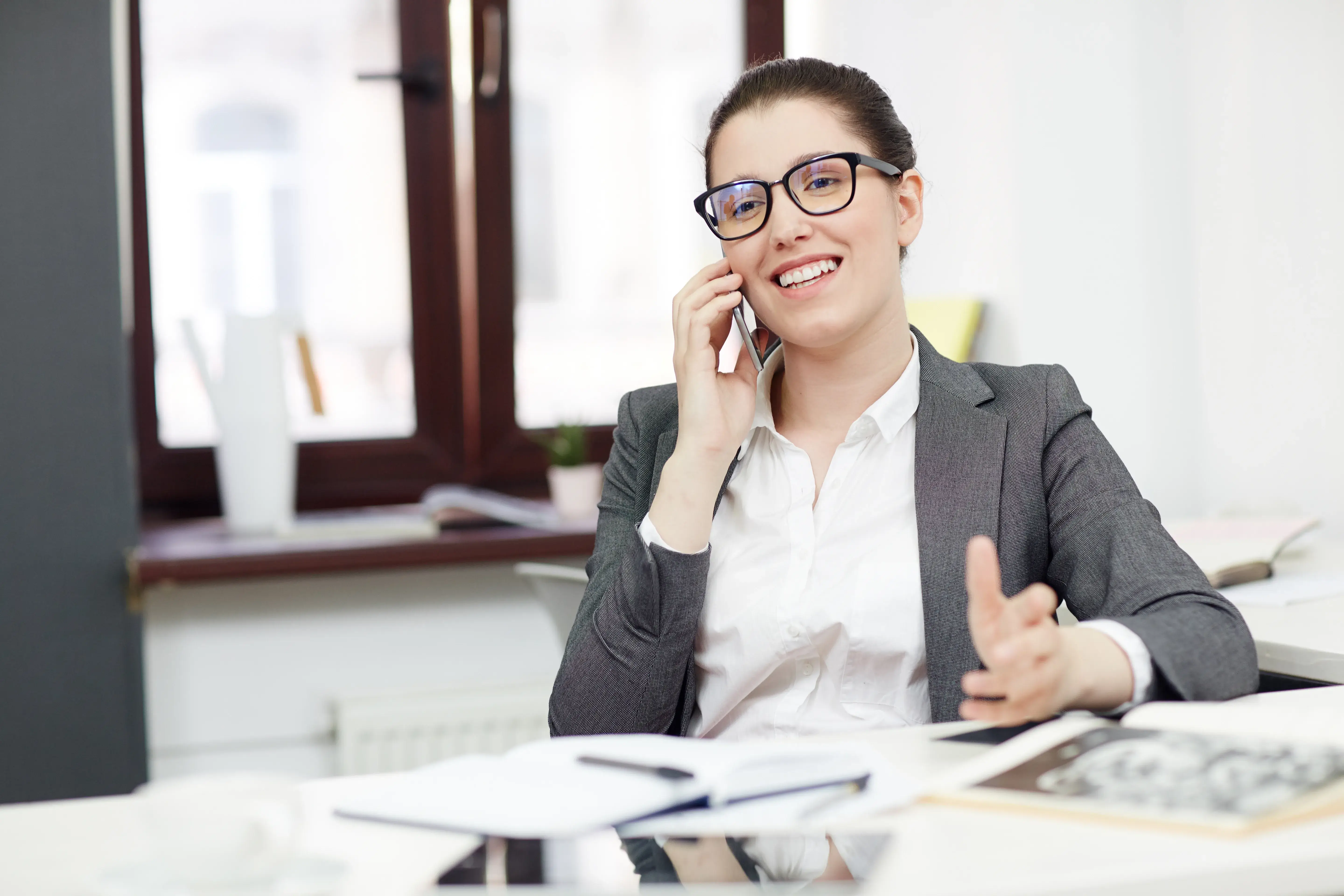 Woman in glasses smiling while talking on a phone in an office