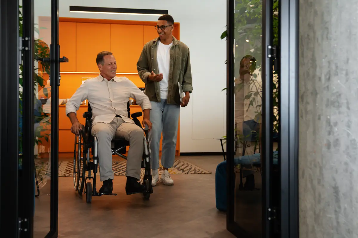 A happy elderly person in a wheelchair entering a vacation rental home and being assisted by a manager.