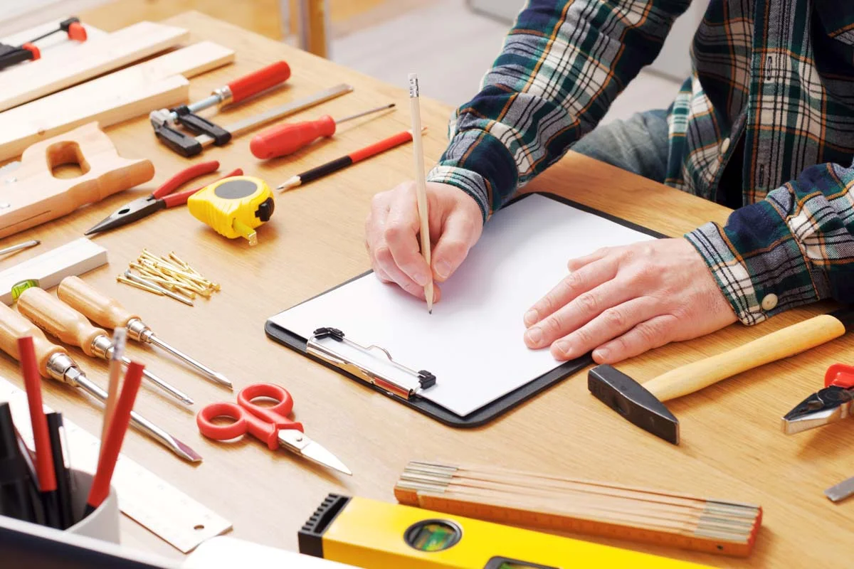 A home maintenance clip board on a desk and basic repair tools laying alongside