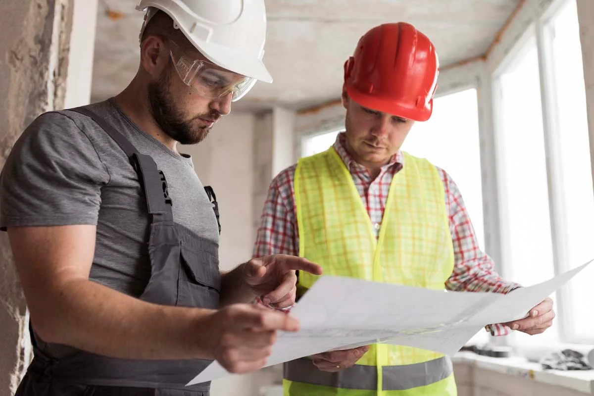 A professional home inspector and a client inspecting the exterior foundation of a house