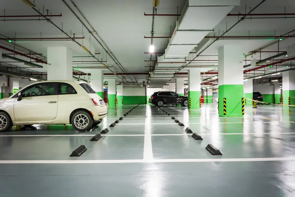 A well-lit underground parking garage with two rows of parked cars facing a central driving lane.