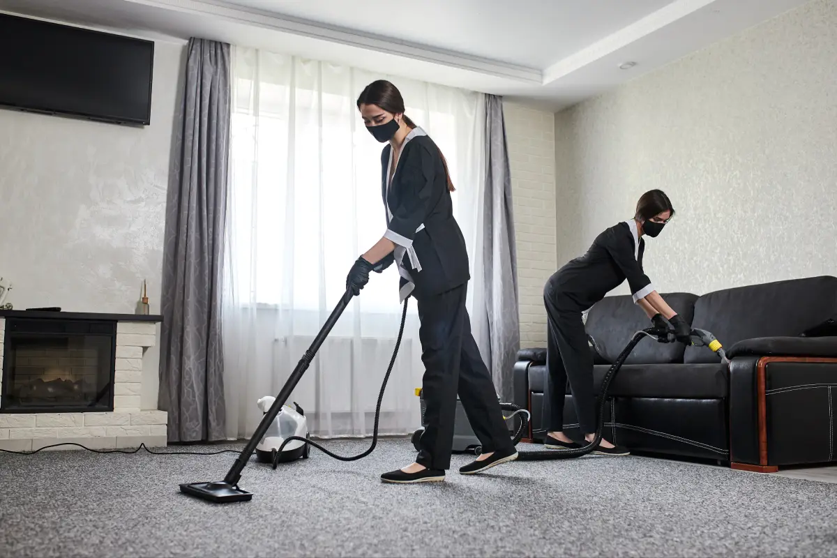 A worker in a hazmat-style suit vacuuming a modern living room floor.