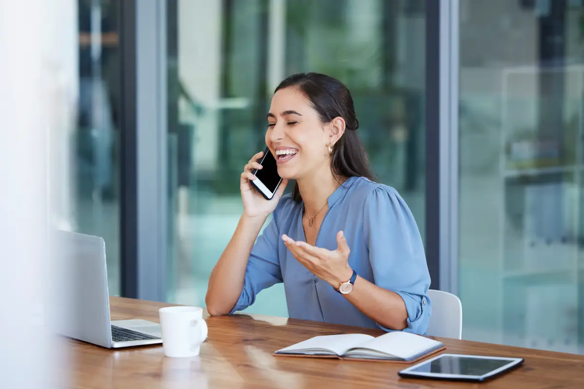 A young woman smiling while on a phone call at her office desk.
