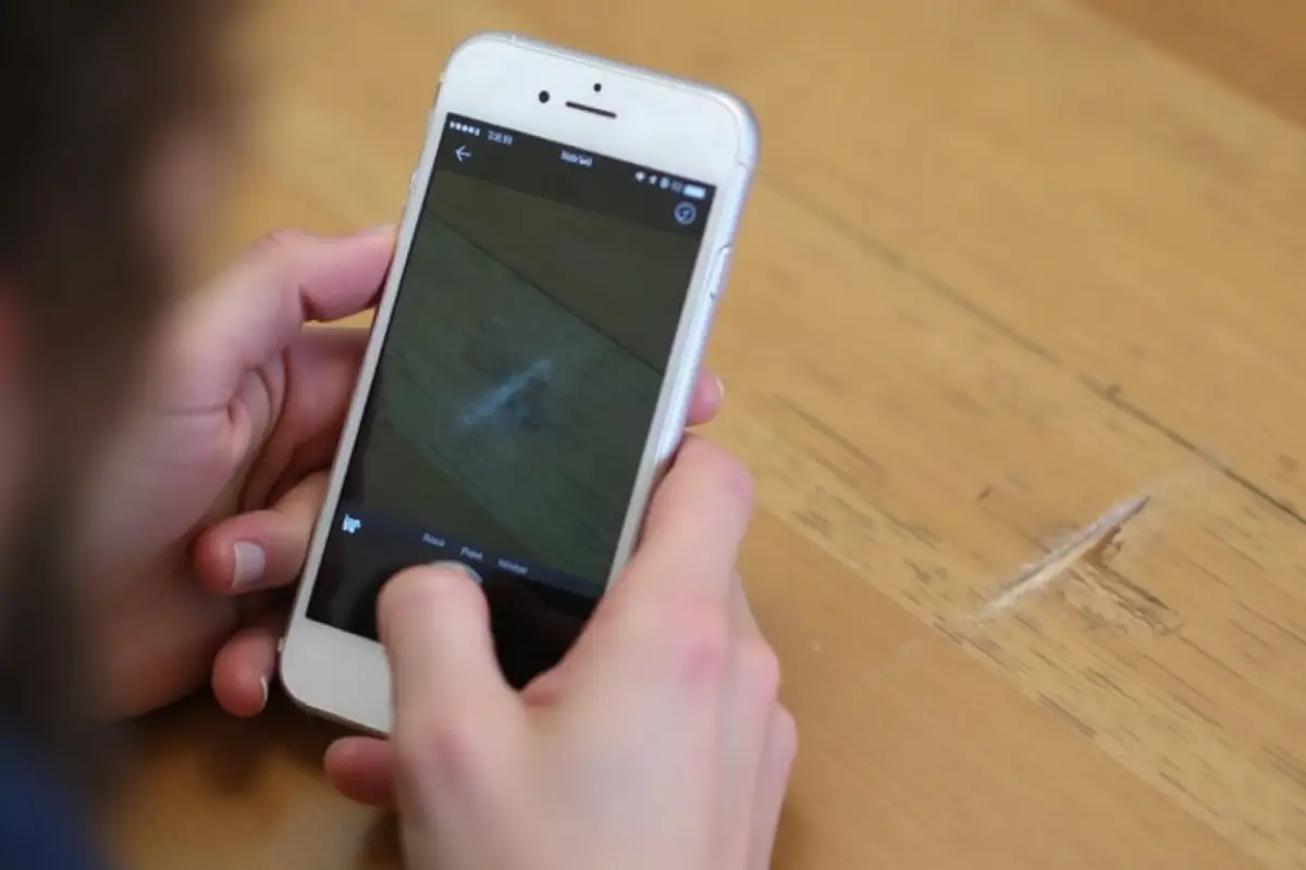Person taking a close-up smartphone photo of damage on a wooden surface for a condition report.
