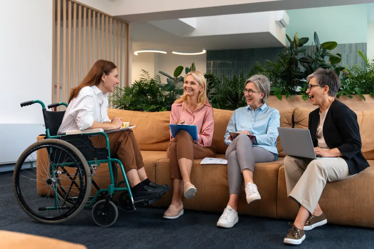 Property manager, homeowner, and a guest in a wheelchair talk together in a bright, open vacation rental living room.